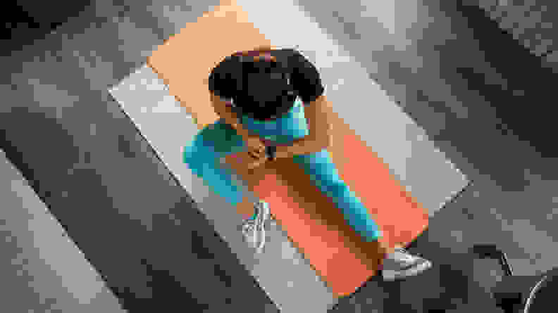 A woman checking her fitness tracker on a yoga mat.