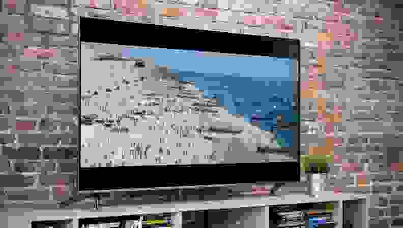 A TCL TV on a media console, showing a scene of a beach war scene.