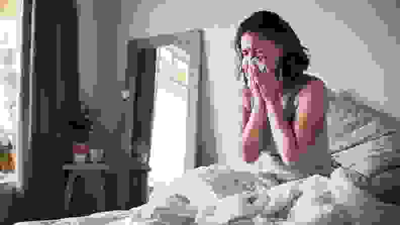 a woman in bed sneezing into a tissue