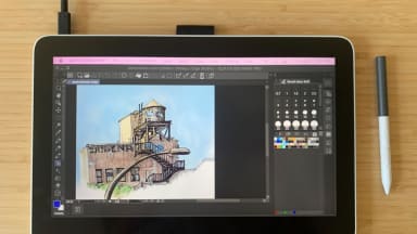 The image shows the Wacom One 13 Touch drawing tablet with Clip Studio Paint pulled up on the screen, showing a digital painting—next to it sits Wacom’s digital pen.