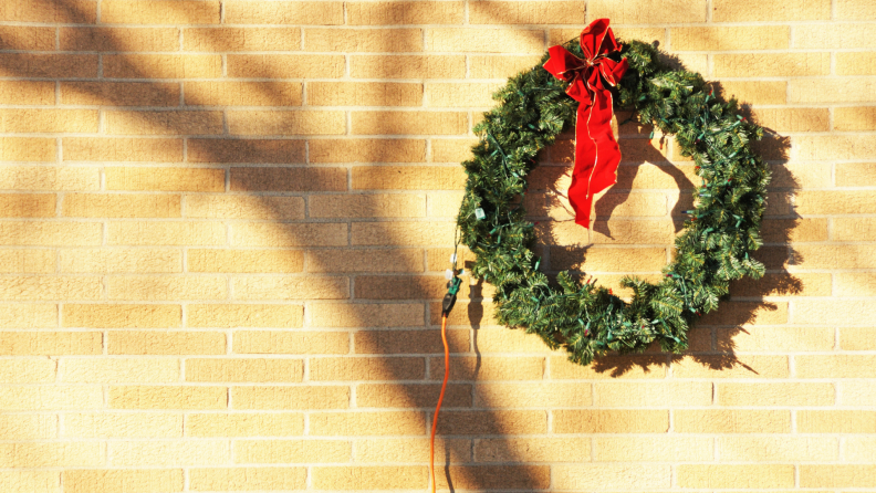Wreath hanging on a brick wall with an extension cord attached.