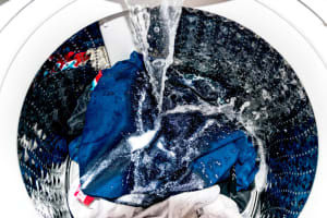 A washing machine being filled with water, with some clothing and powder detergent inside
