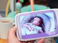 Person holding baby monitor in front of cup of coffee with sleeping baby monitor on screen.