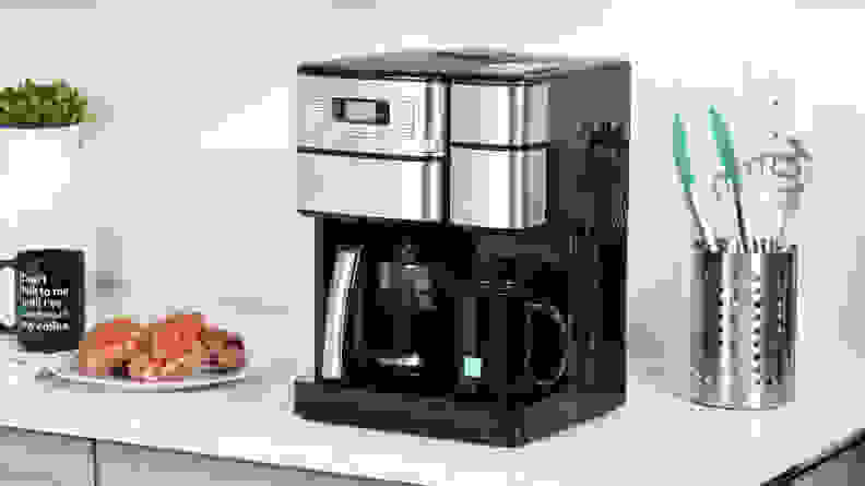 The silver and black Cuisinart coffee machine on a counter next to a coffee mug and plate of pastries.