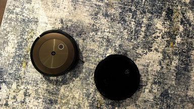 Two robot vacuums sit on a gray rug