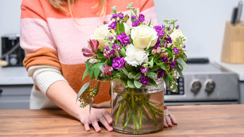 A person standing behind a vase of flowers on a countertop.