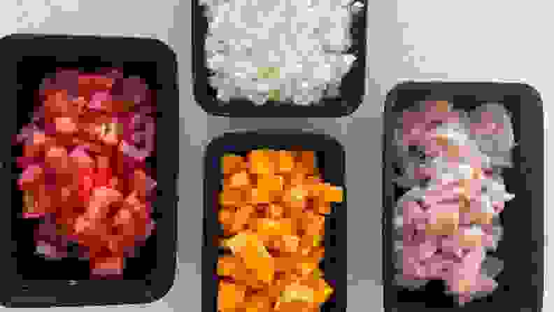 Four black plastic containers filled with diced tomato, sweet potato, onion, and raw chicken.