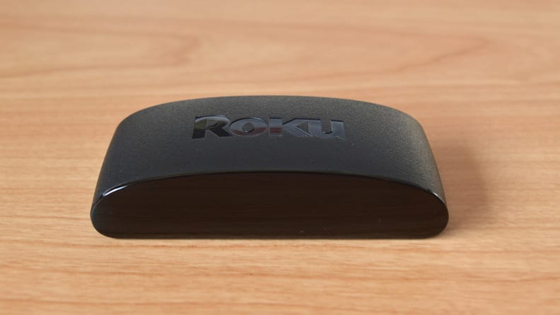 The Roku Express 4K+ sits as a rounded black box atop a light, woodgrain surface.