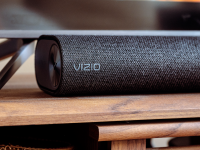 A fabric covered black Vizio soundbar sits below a TV on a wooden console.