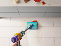 The Dyson Submarine wet roller head cleans up a messy stain on a white kitchen floor.