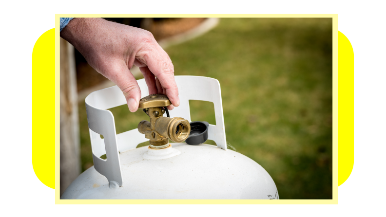 Person using fingers to turn knob on the top of a propane tank outdoors.