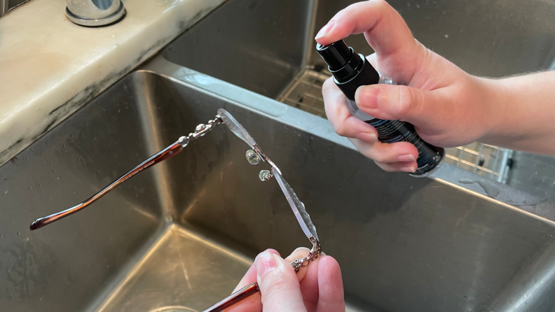 Author spraying glasses cleaner on glasses over sink