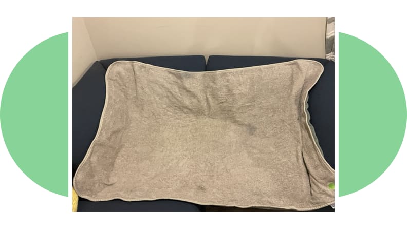 A gray Peapod bedwetting mat on top of navy colored couch in front of wall indoors.