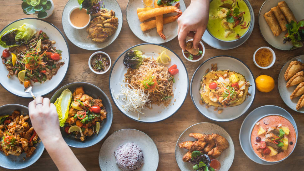 On a dinner table, dishes of various styles and cuisines are on display, including shrimp tempura(shrimp fried in batter), nasi goreng, and Thai green curry.