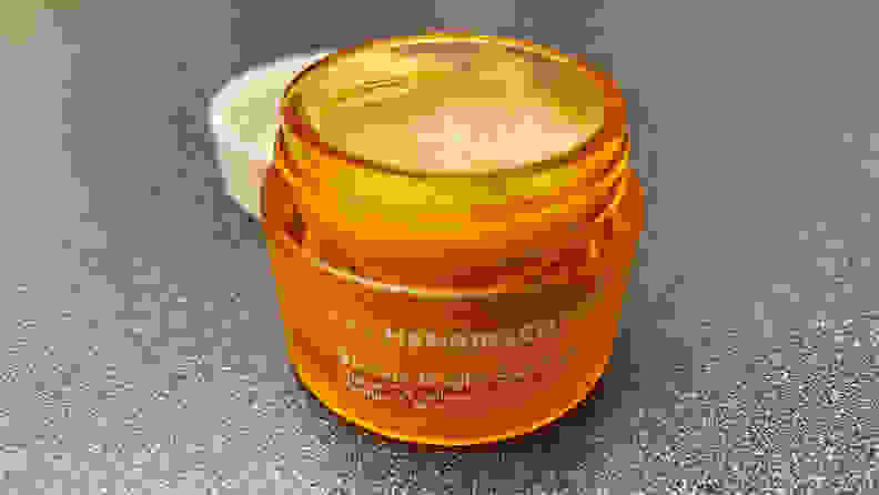 The OleHenriksen Banana Bright Eye Crème sitting on a bathroom vanity with its lid off to expose a orange-tinted cream.