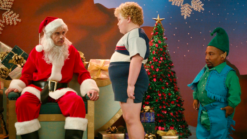 In Bad Santa (2003), Billy Bob Thornton adorned in a red Santa outfit glares at a large child while an unhappily elf-dressed Tony Cox observes.