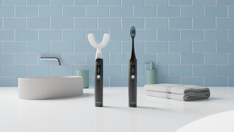 A modern bathroom scene featuring a sleek Y-Brush toothbrush with a U-shaped head alongside a traditional electric toothbrush, set against a clean blue tiled backdrop with a minimalist sink and neatly folded towels.