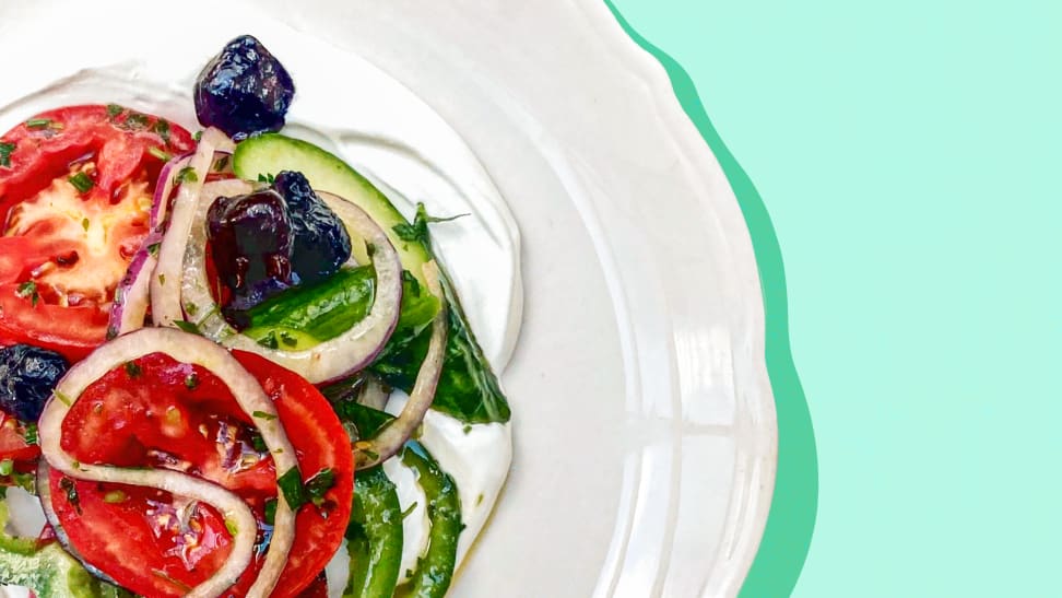 A Greek salad on a white plate on a wood surface.