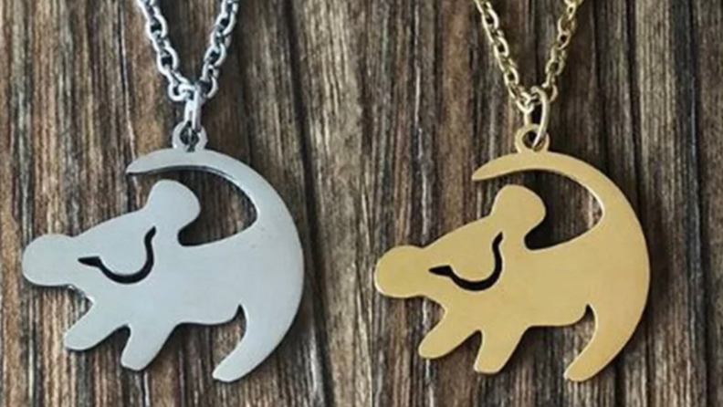Two necklaces side-by-side featuring a Simba charm. One is gold, one is silver.