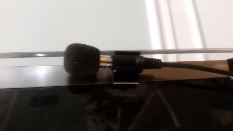 An image of the microphone of the Pocketalker Ultra D1 resting on a table with its extension cord connecting outside of frame.