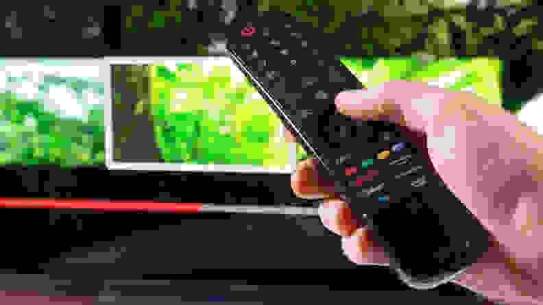 A person changes a channel using a TV remote for an LG OLED TV.