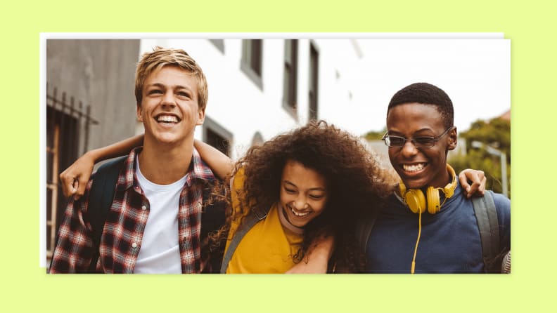 A teen boy, a teen girl, and another teen boy walking on the side of a street and smiling.