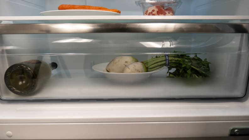 A close-up of the fridge's singular crisper drawer, with a root vegetable in it for scale.