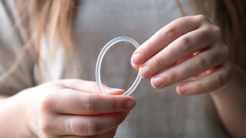 Person holding clear hormonal contraceptive ring in hands.