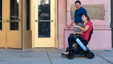 A person uses a Whill wheelchair to travel alongside a walking companion.