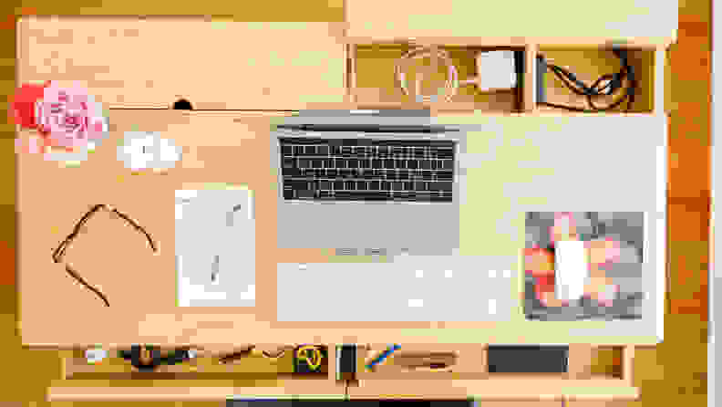 The top of a desk showing a computer, a pair of glasses, and a vase of flowers