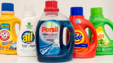 Five bottles of liquid laundry detergent stand in a row