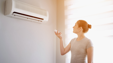 Person using remote to control air conditioner unit mounted on wall.