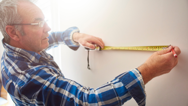 A person measures a stretch of wall with a measuring tape.