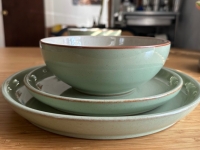 A stack of teal dinnerware with orange rims. The stack has one dinner plate, one salad plate, and a cereal bowl.