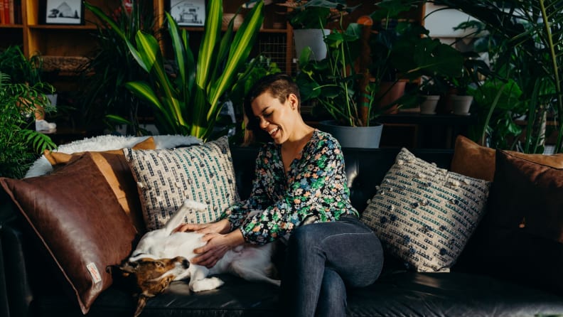 A woman pets her dog in a room of plants.