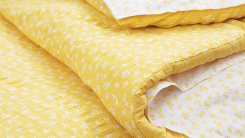 A yellow comforter cloaks white floral sheets.
