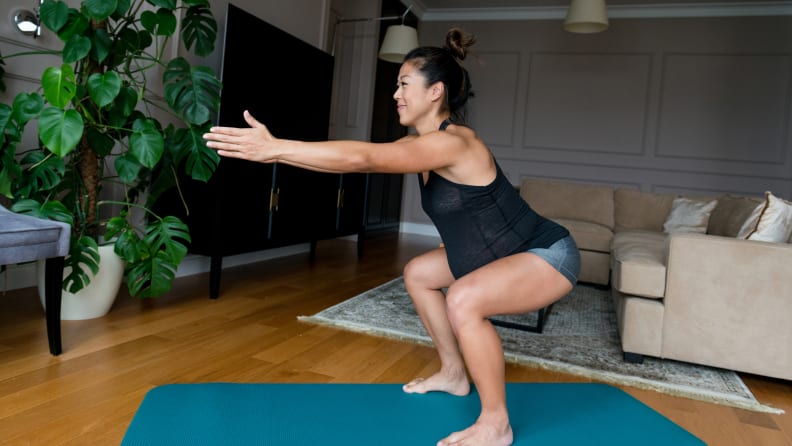 Active pregnant woman holds a squat position while exercising in her home.