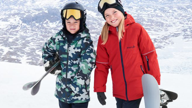 Two young kids in the snow wearing ski parkas and carrying skis