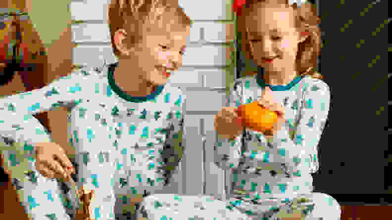 A boy and a girl sitting by a fireplace peeling an orange.