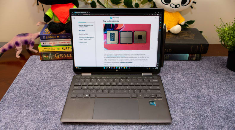 An open laptop on a desk, with books and tchotchkes in the background