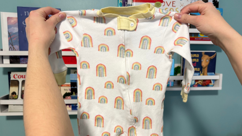 A person holding a Burt's Bees Baby onesie, with rainbows all it.