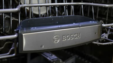 A close-up of the front of a Bosch dishwasher's top rack, which has the Bosch logo on it.
