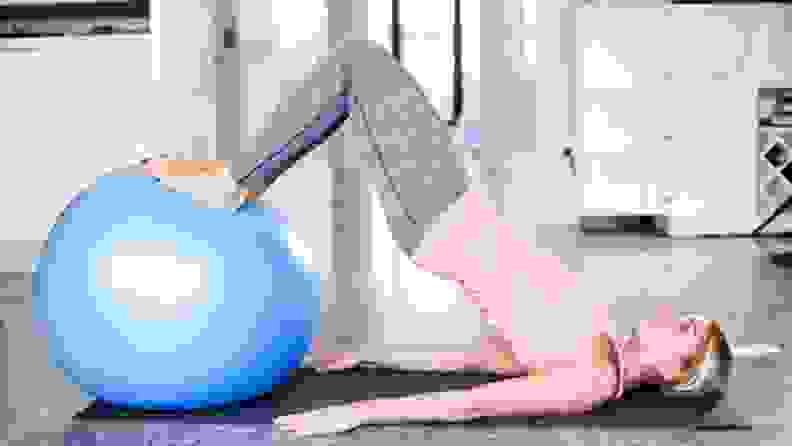 A woman in workout gear uses a blue yoga ball to do abdominal work.