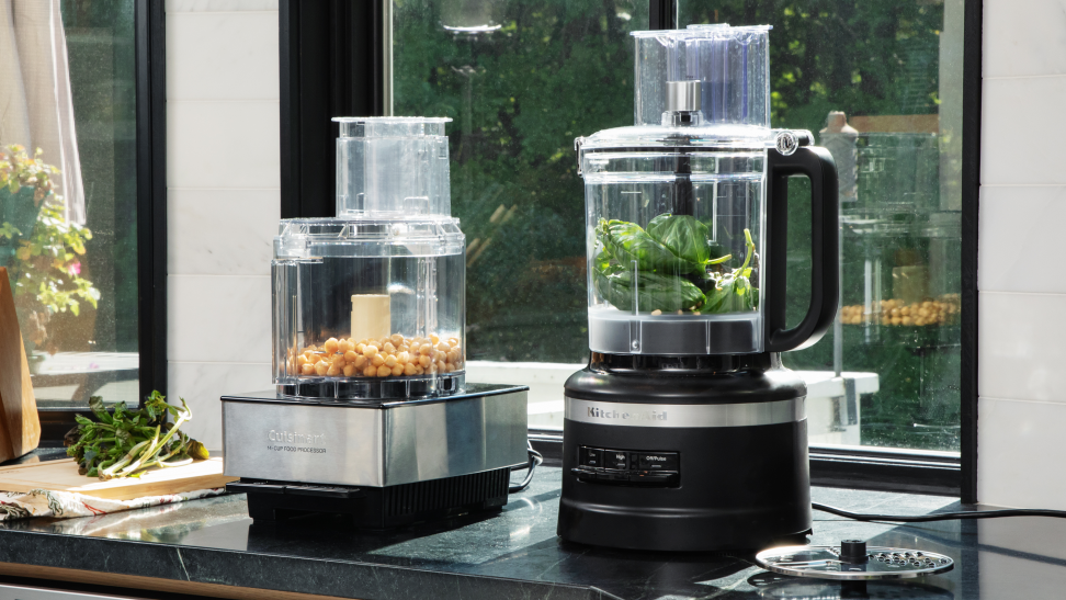 Cuisinart and KitchenAid food processors filled with ingredients and placed on a countertop in front of a window