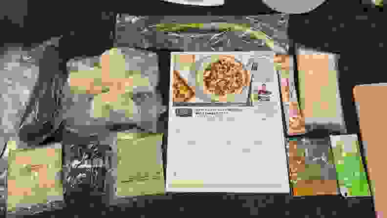 Several plastic packages of produce and spices, plus a recipe card, laid out on a countertop
