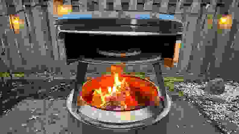 Solo Stove Pi Fire pizza oven with open flame outdoors with pizza cooking inside.