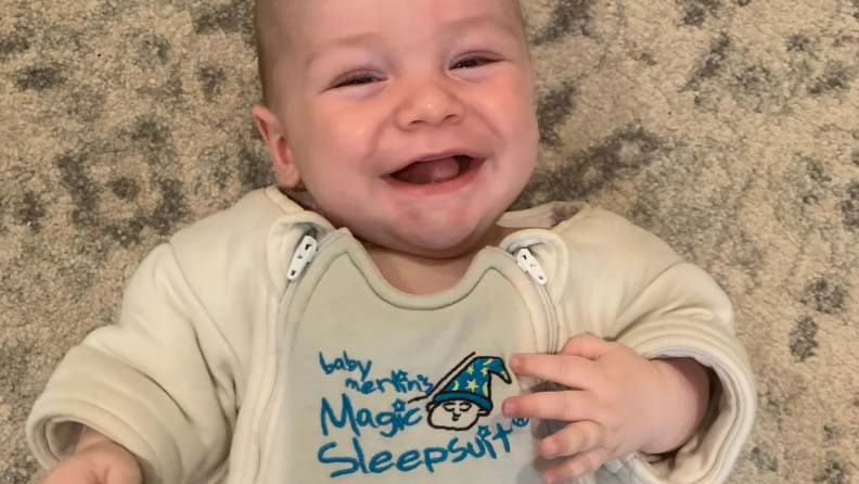 A baby smiles as it's swaddled in a Magic Merlin sleepsuit.