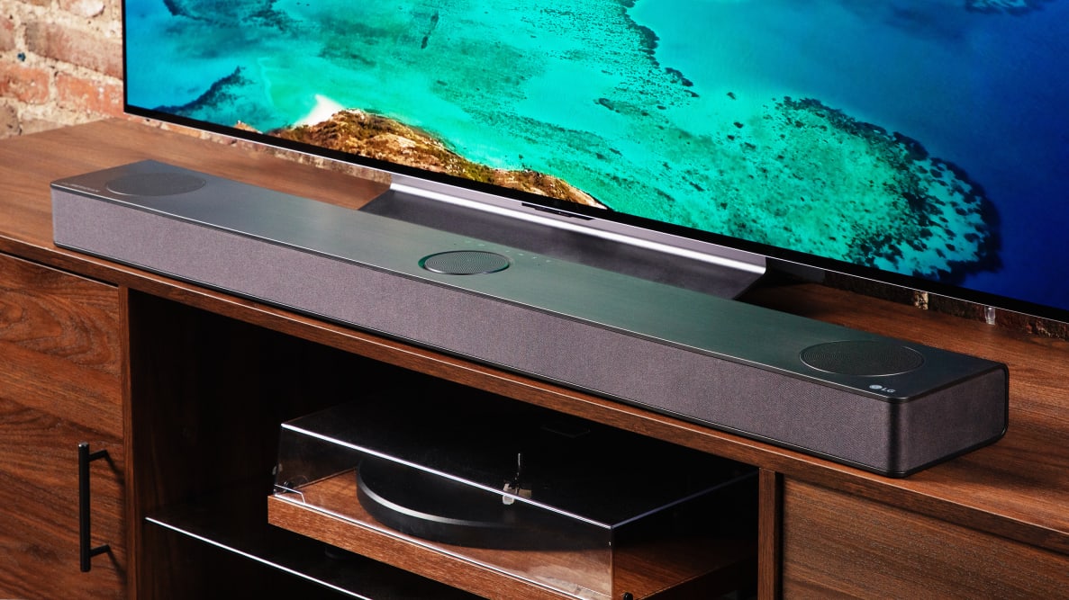 An LG S80QY soundbar sits on a TV stand next to a television.