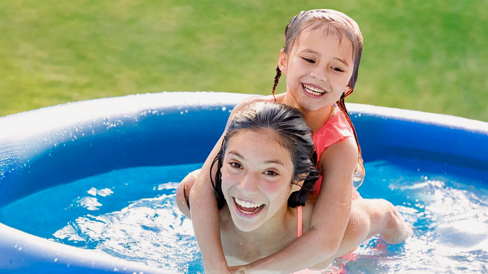 A pair of happy swimmers enjoy the Intex Easy Set, a round blue inflatable pool resting in the grass.