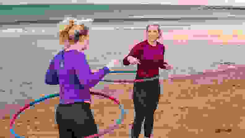 Two women hula hooping on a beach.